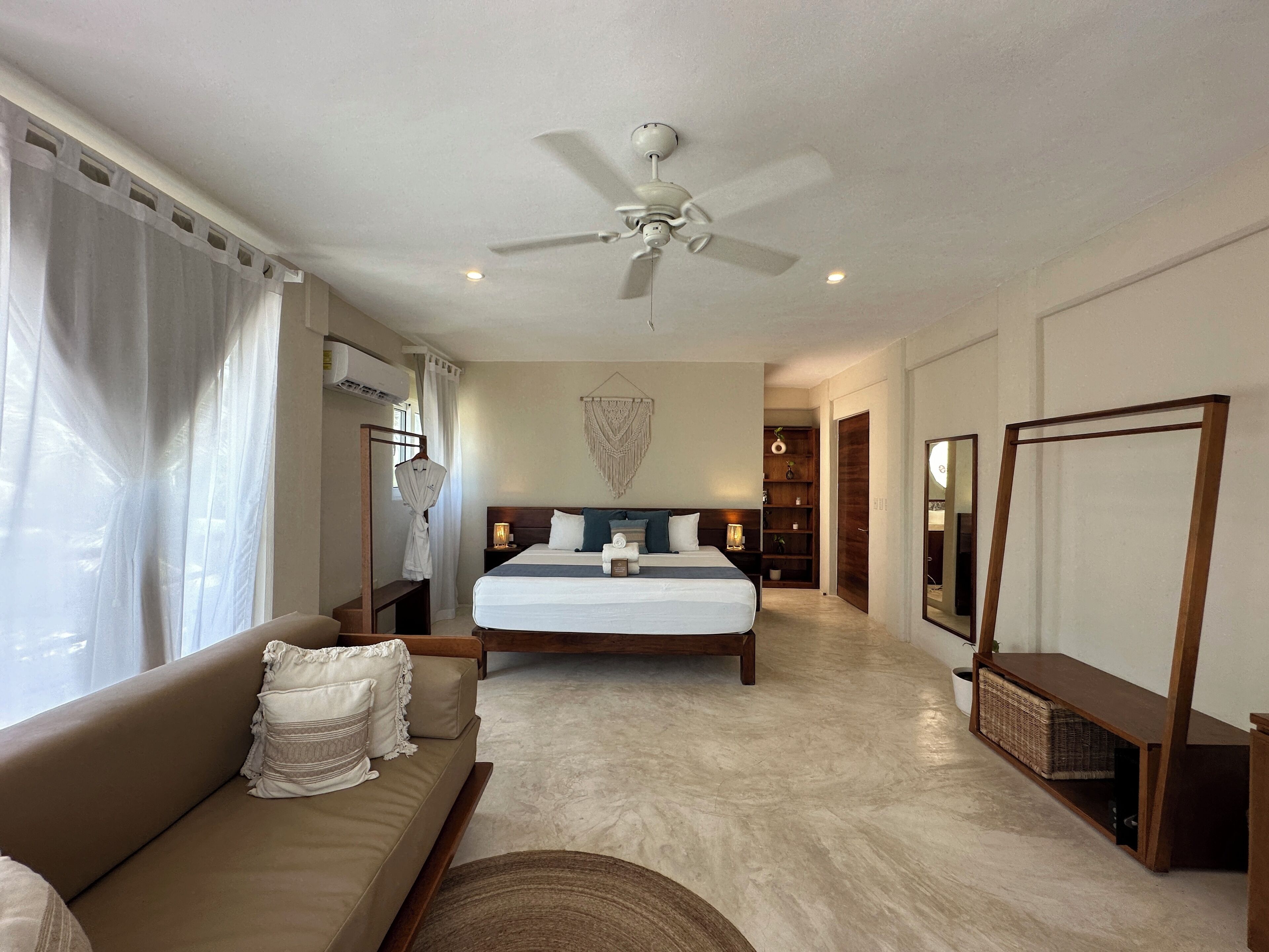 Habitación de hotel con cama, sofá, ventilador de techo, espejo y una pequeña mesa.
