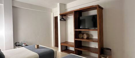 A hotel room with two beds, a ceiling fan, a TV on a wooden shelf, and a small table with a kettle and cups.