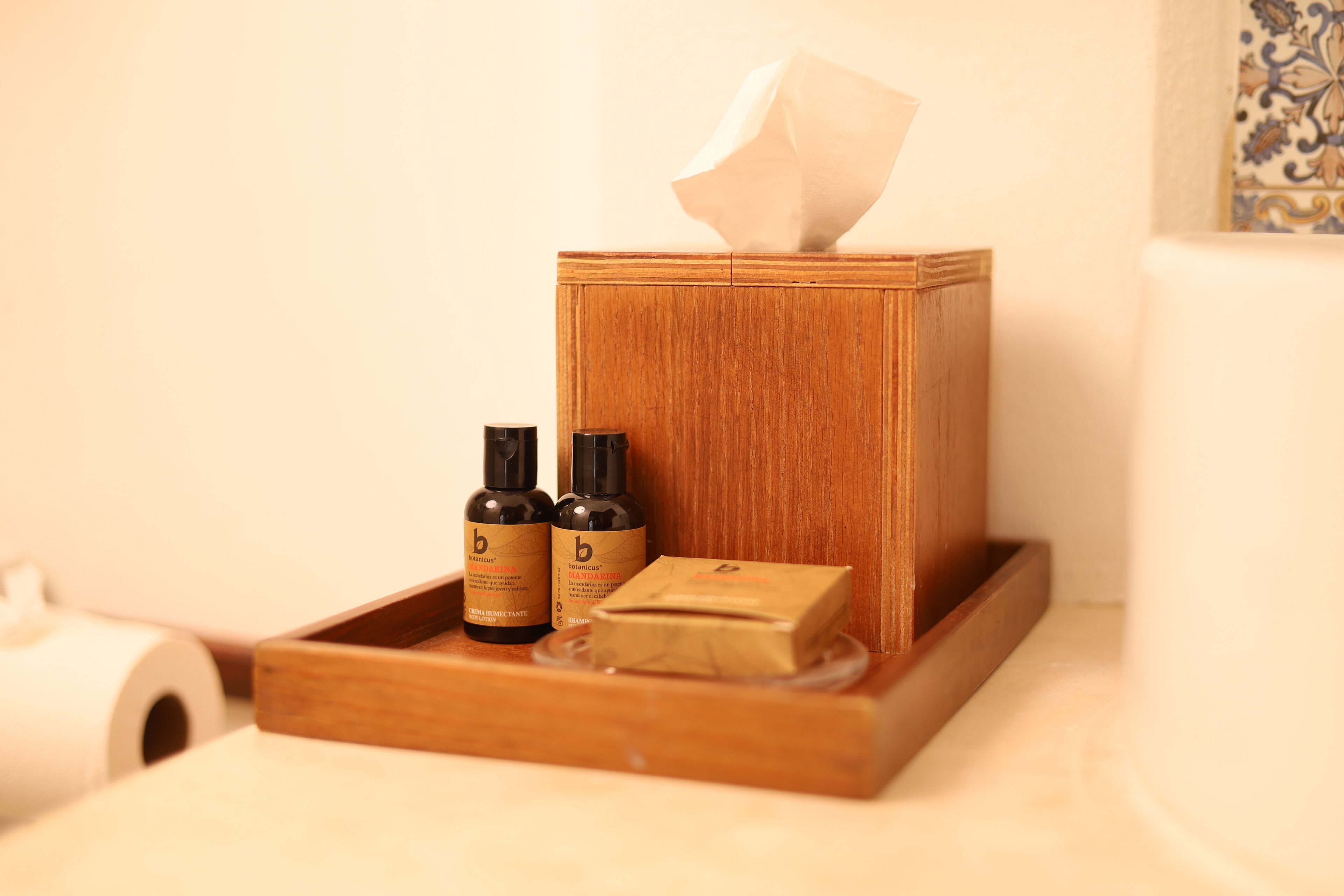 A wooden tissue box with two bottles of lotion and a bar of soap on a tray.