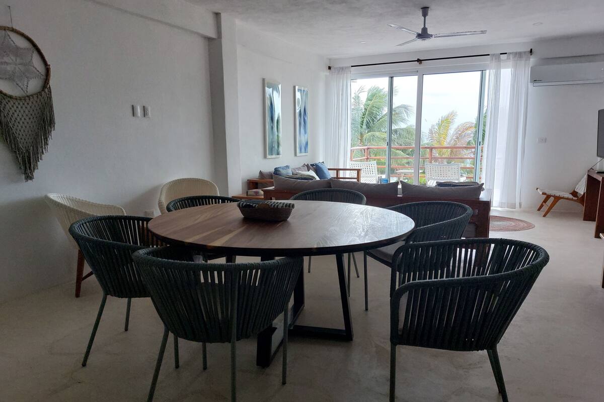 Ein modernes Wohnzimmer mit einem runden Holztisch, umgeben von Korbstühlen, einer Couch und einem Fernsehtisch.