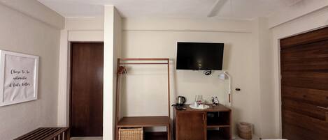 Quarto com cama, ventoinha no teto, televisão, escrivaninha com abajur e guarda-roupa de madeira.