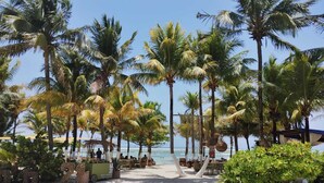 A beachside resort with palm trees, outdoor seating, and a view of the ocean. - Noah Beach Hotel & Suites (Mahahual)