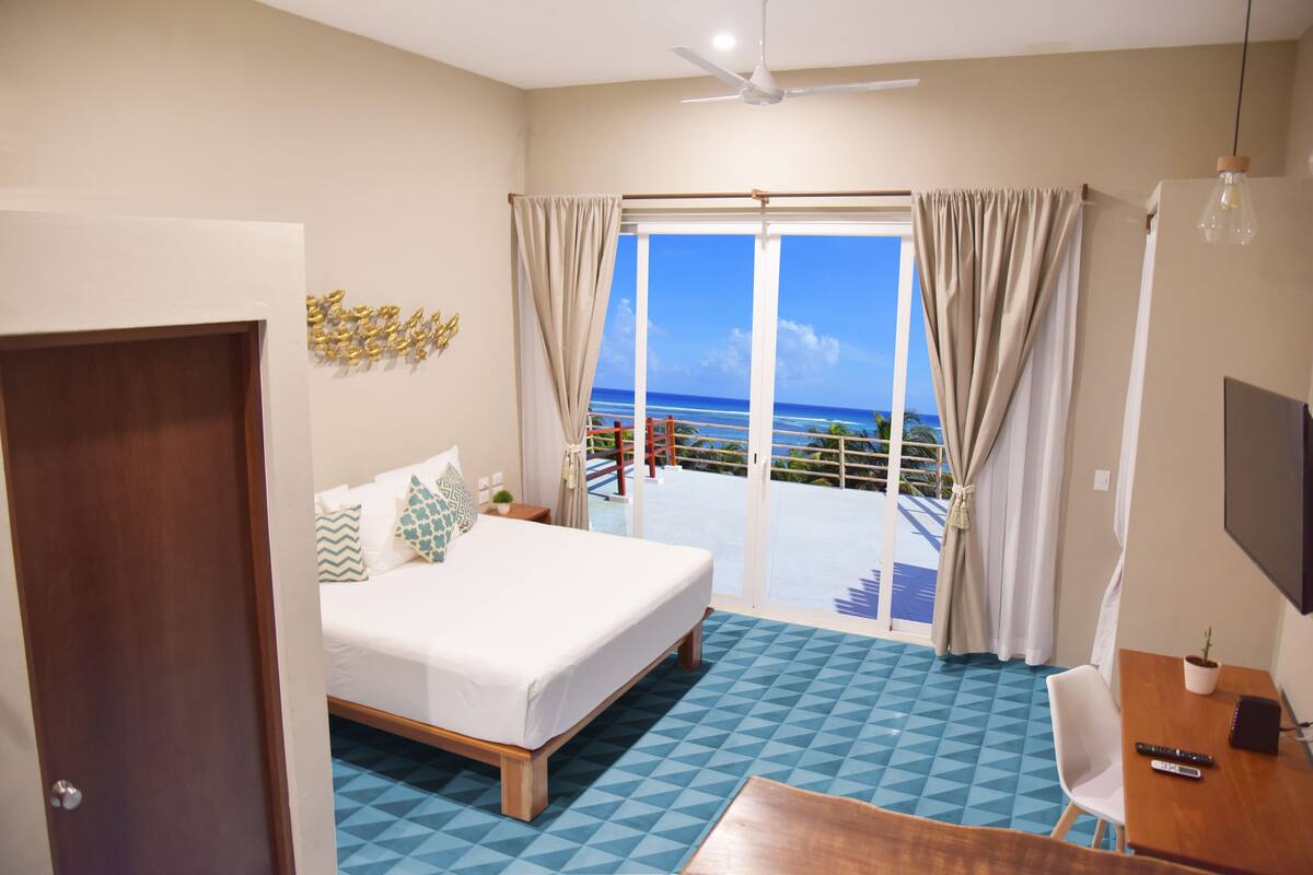 Ein Hotelzimmer mit Bett, Schreibtisch, Stuhl, Fernseher und einem Balkon mit Meerblick.