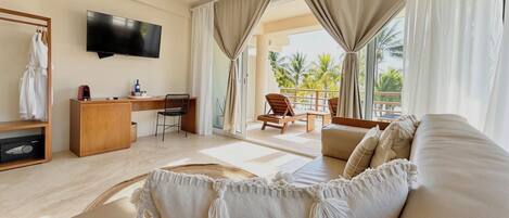 A hotel room with a sofa, a desk, a TV, and a balcony with chairs.
