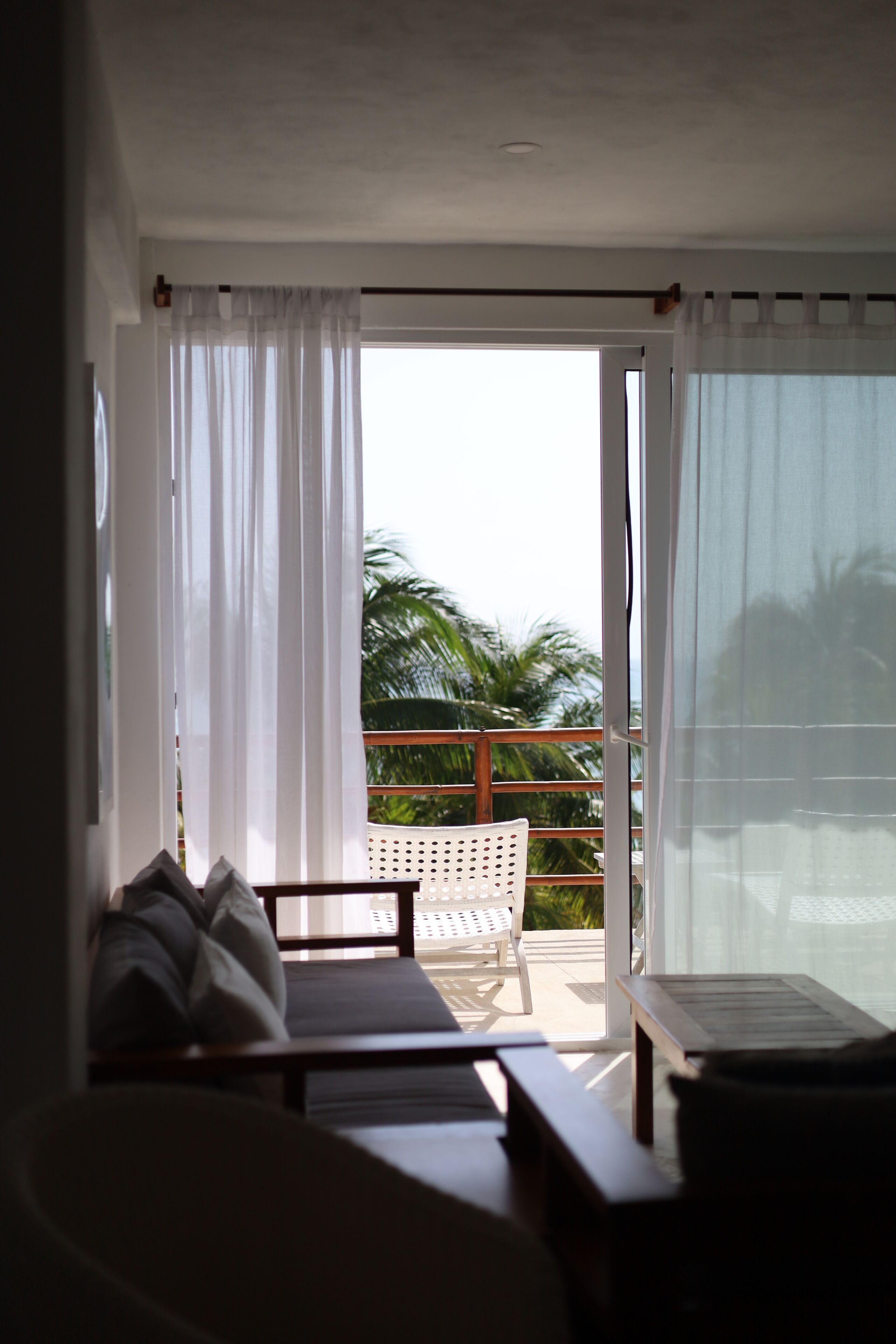 Ein Zimmer mit einer Couch, einem Tisch und Blick auf einen Balkon mit einer Palme.