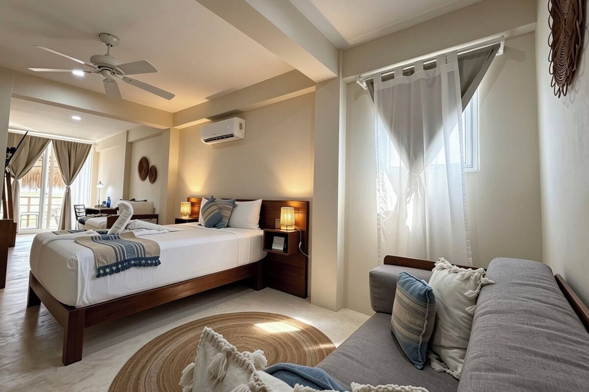 Ein Hotelzimmer mit Bett, einer Sitzecke, Deckenventilator, Klimaanlage und einem Vorhangfenster.