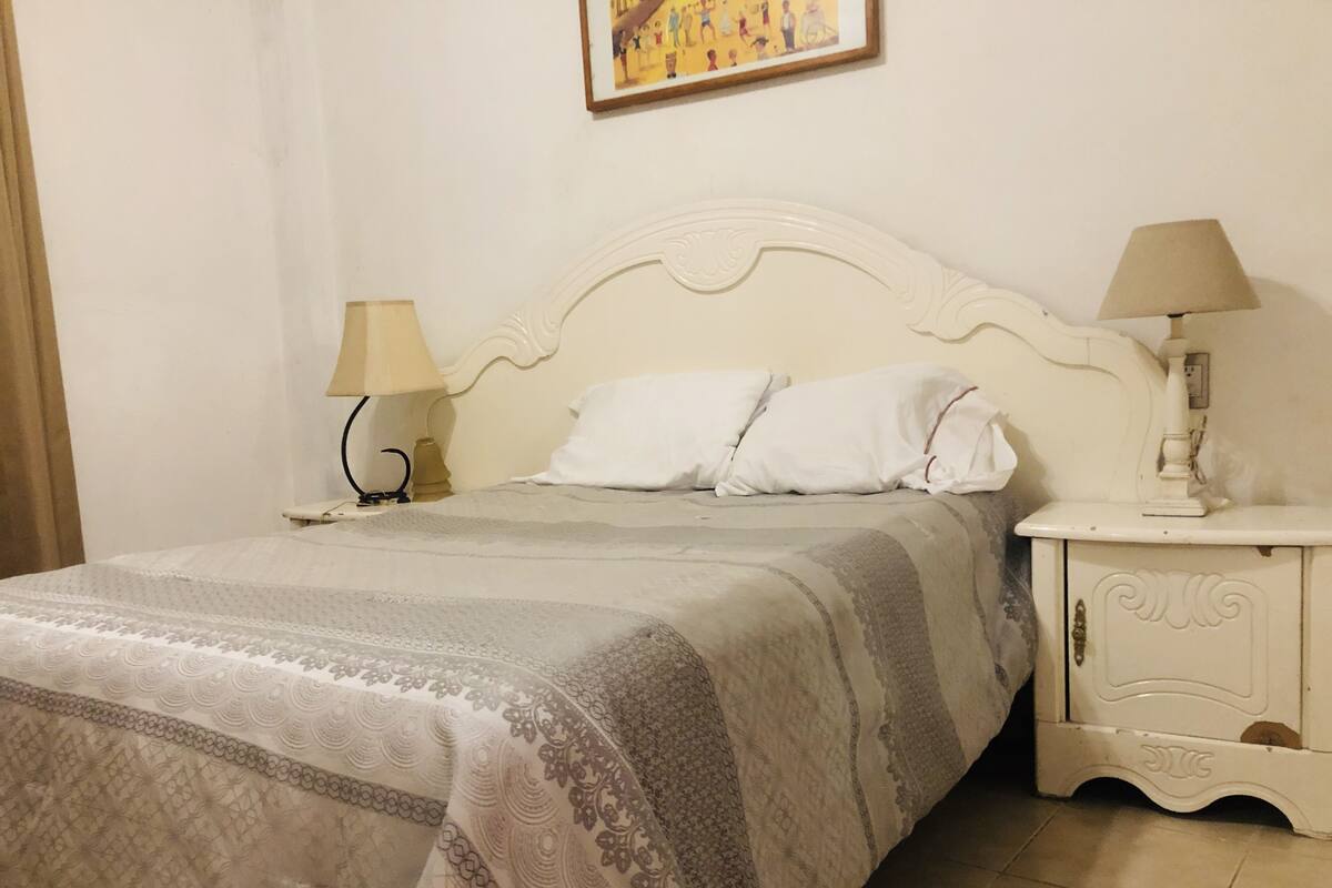 A neatly made bed with a patterned bedspread, two bedside lamps, and a small white nightstand with a lamp.