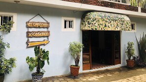 Un bâtiment sur lequel on peut lire les inscriptions « EL CAPRICHO » et « XICOTEPEC », avec une flèche pointant vers la droite. Devant, on trouve des plantes en pot, et au-dessus de l’entrée, une grande marquise décorative.
