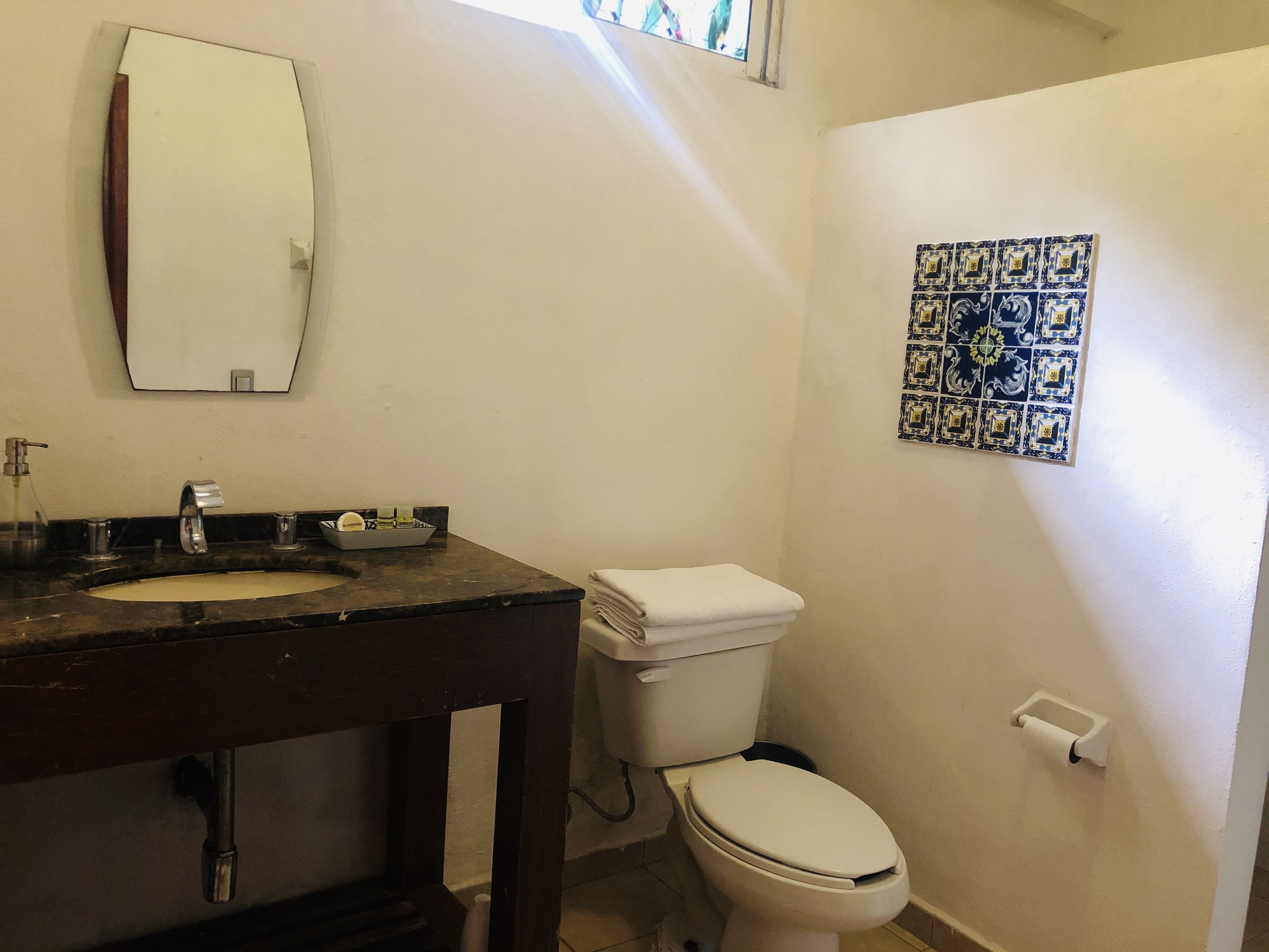 Un baño con lavabo, espejo, inodoro y pared decorada con azulejos.