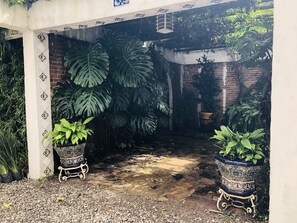Un espace extérieur aménagé en jardin, avec de grands pots de plantes, un mur en briques et un sol carrelé.