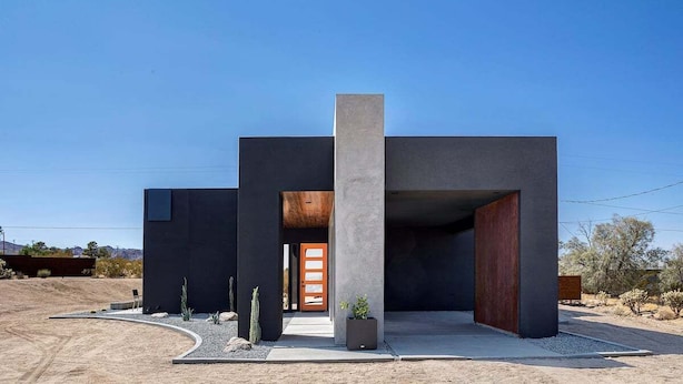 Un edificio moderno con fachada oscura, una columna central de hormigón y una puerta de madera.
