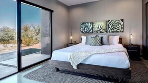Un dormitorio moderno con una cama grande, una puerta corrediza de vidrio a un patio y vistas al desierto.