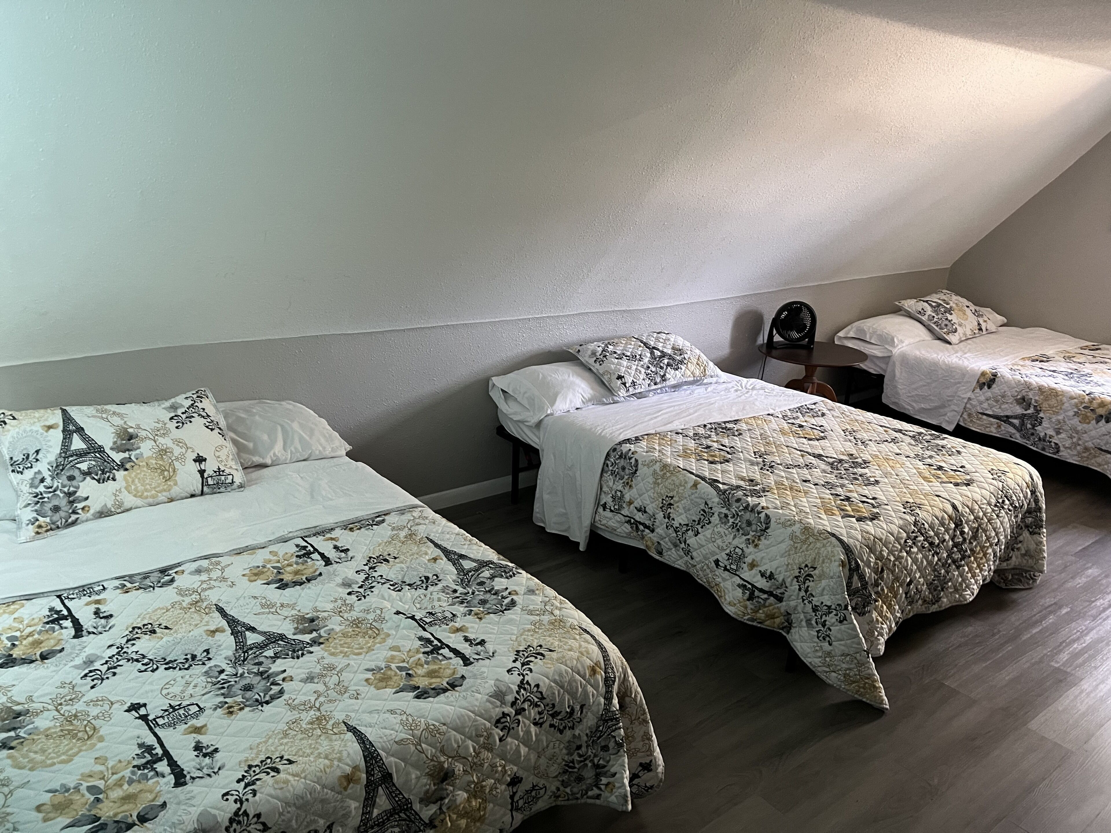 Una habitación con tres camas, cada una con ropa de cama con motivos florales y de la Torre Eiffel.