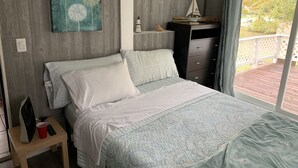 Een slaapkamer met een bed, nachtkastje, kapstok, schilderij en uitzicht op de omgeving.