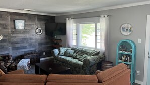 Een woonkamer met een grijze wand met houttextuur, een groene sofa met patroon, een bruine bank, een bijzettafeltje en een blauwgroene boekenkast.