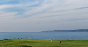 Um campo de golfe com vista para o mar e uma costa distante.