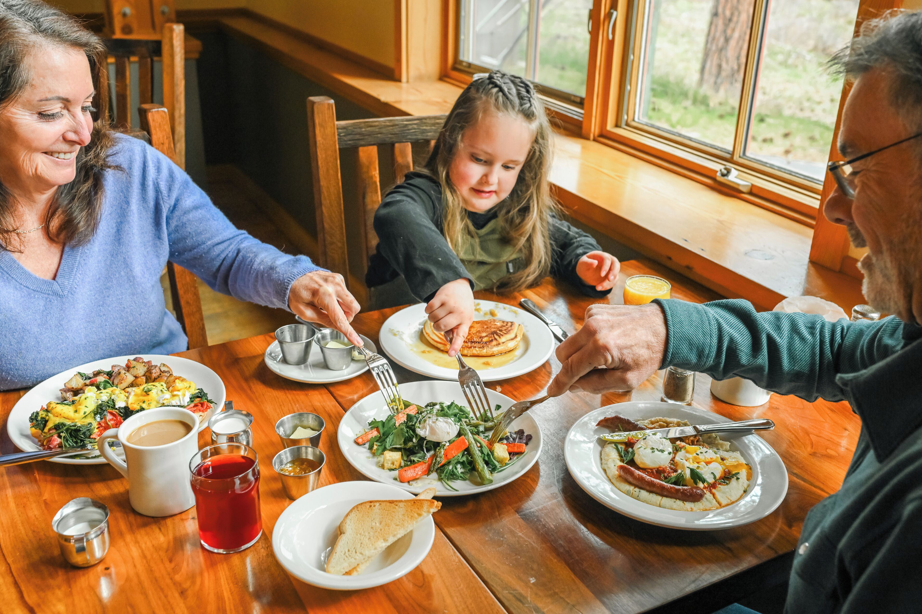 Una famiglia che cena a un tavolo di legno con diversi piatti, tra cui pancake e insalata.