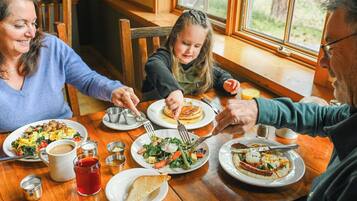 Una famiglia che cena a un tavolo di legno con diversi piatti, tra cui pancake e insalata.
