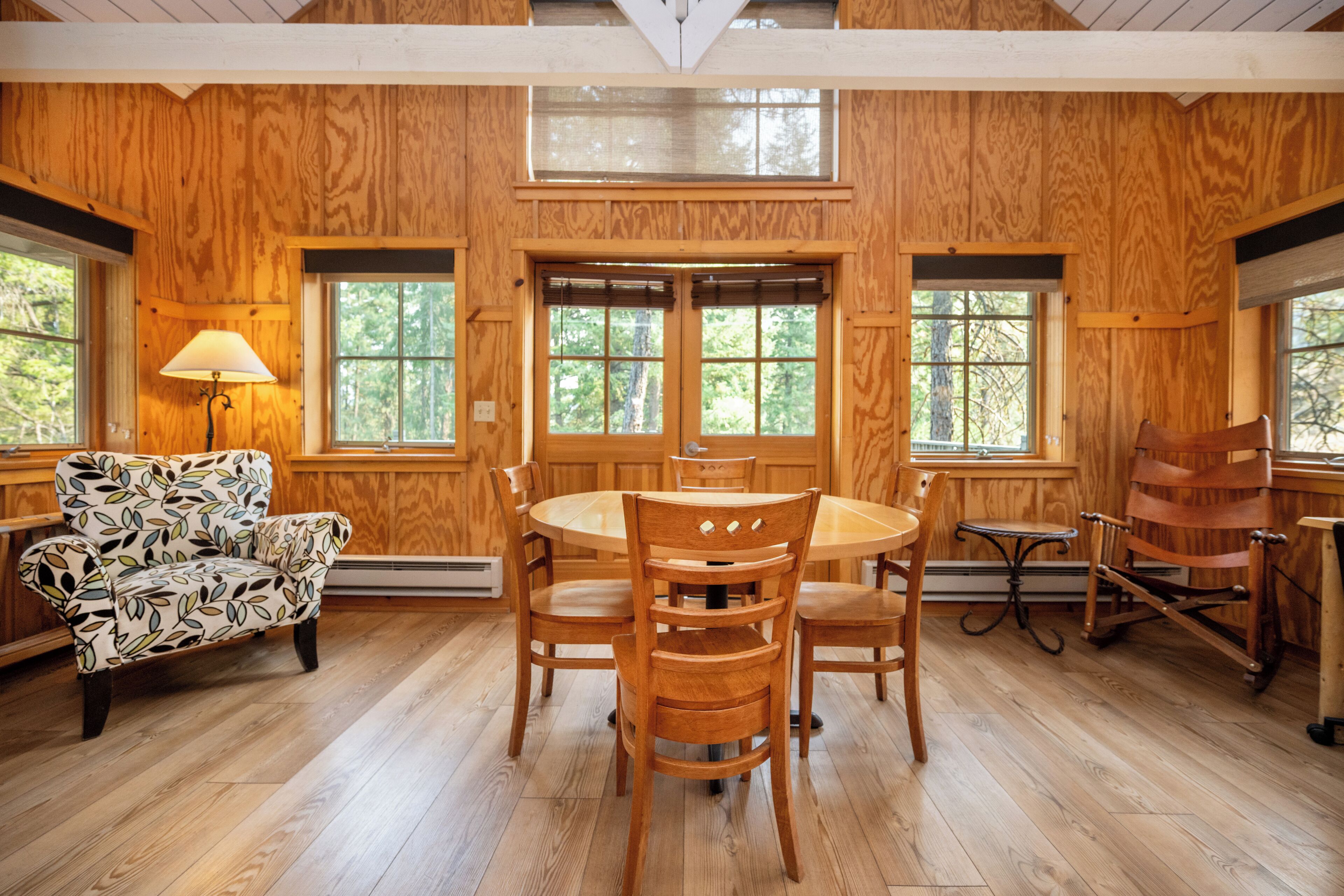 A wooden-paneled room with a round dining table, chairs, and a patterned armchair.