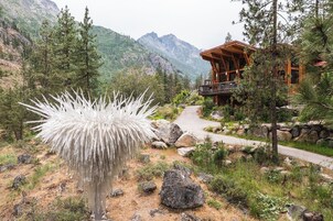 Una cabaña con fachada de madera, rodeada por un paisaje montañoso y una planta blanca distintiva en primer plano.