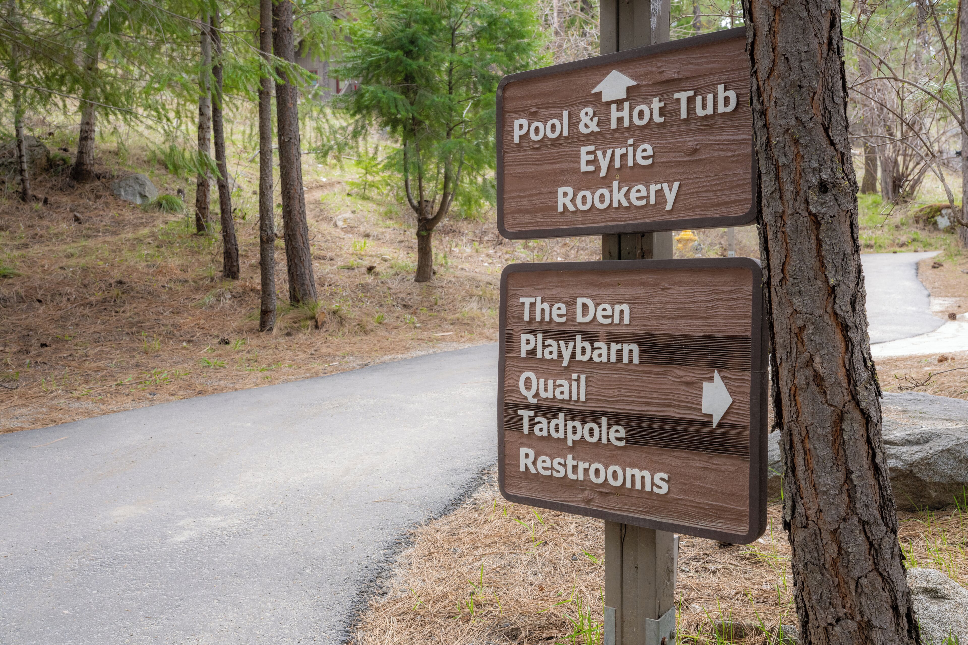 A directional sign with arrows pointing to amenities such as Pool & Hot Tub, Eyrie Rookery, The Den, Playbarn, Quail, Tadpole, and Restrooms.