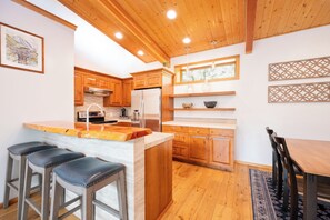 A modern kitchen with wooden cabinets, a central island, bar stools, and a dining table.
