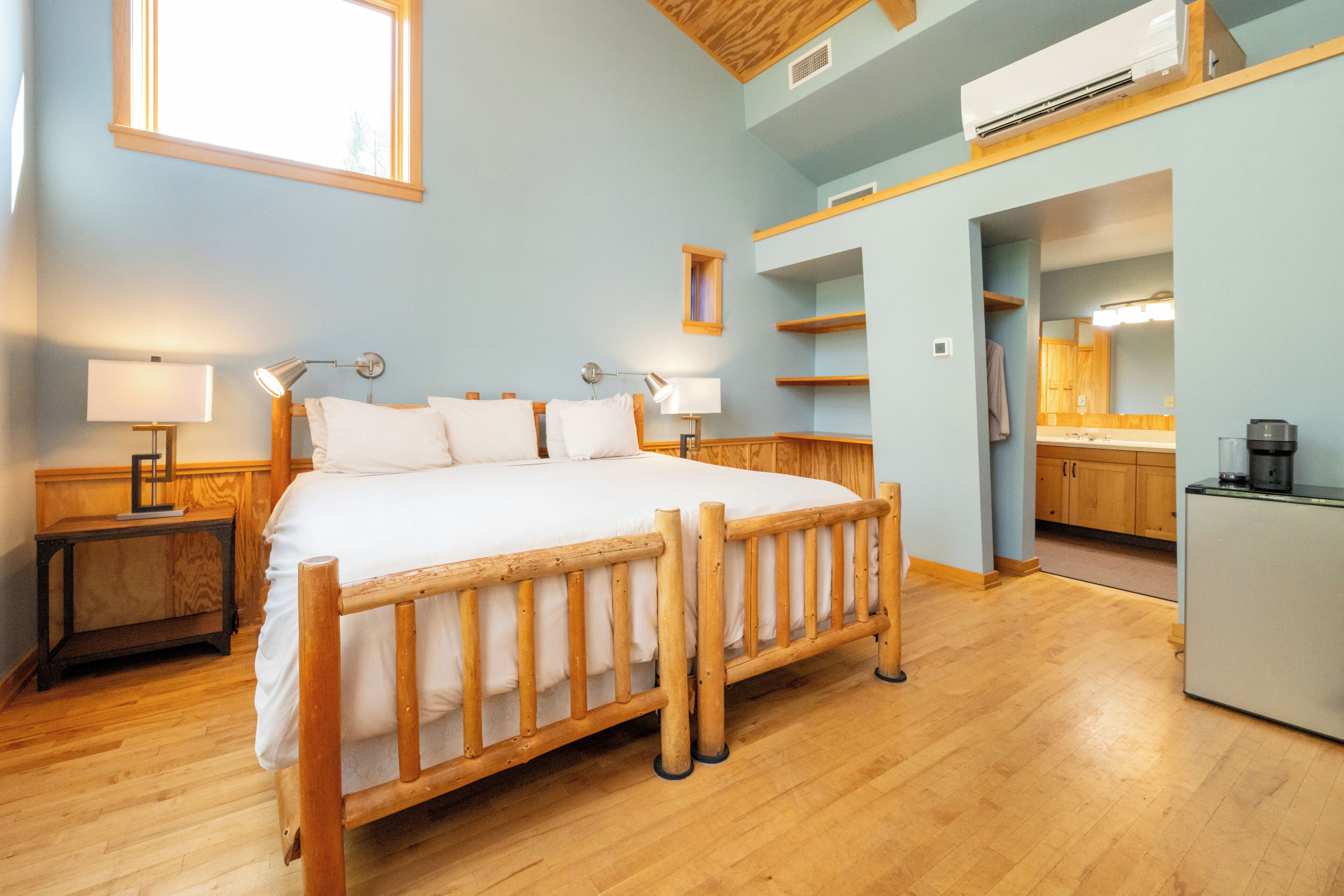 A bedroom with a wooden bed, two bedside tables with lamps, a built-in wardrobe, and a kitchenette area.