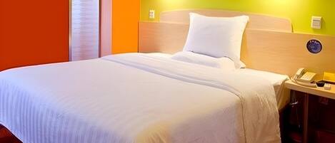 Ein Hotelzimmer mit einem großen Bett, einem Nachttisch mit Telefon und einer Wandleuchte.