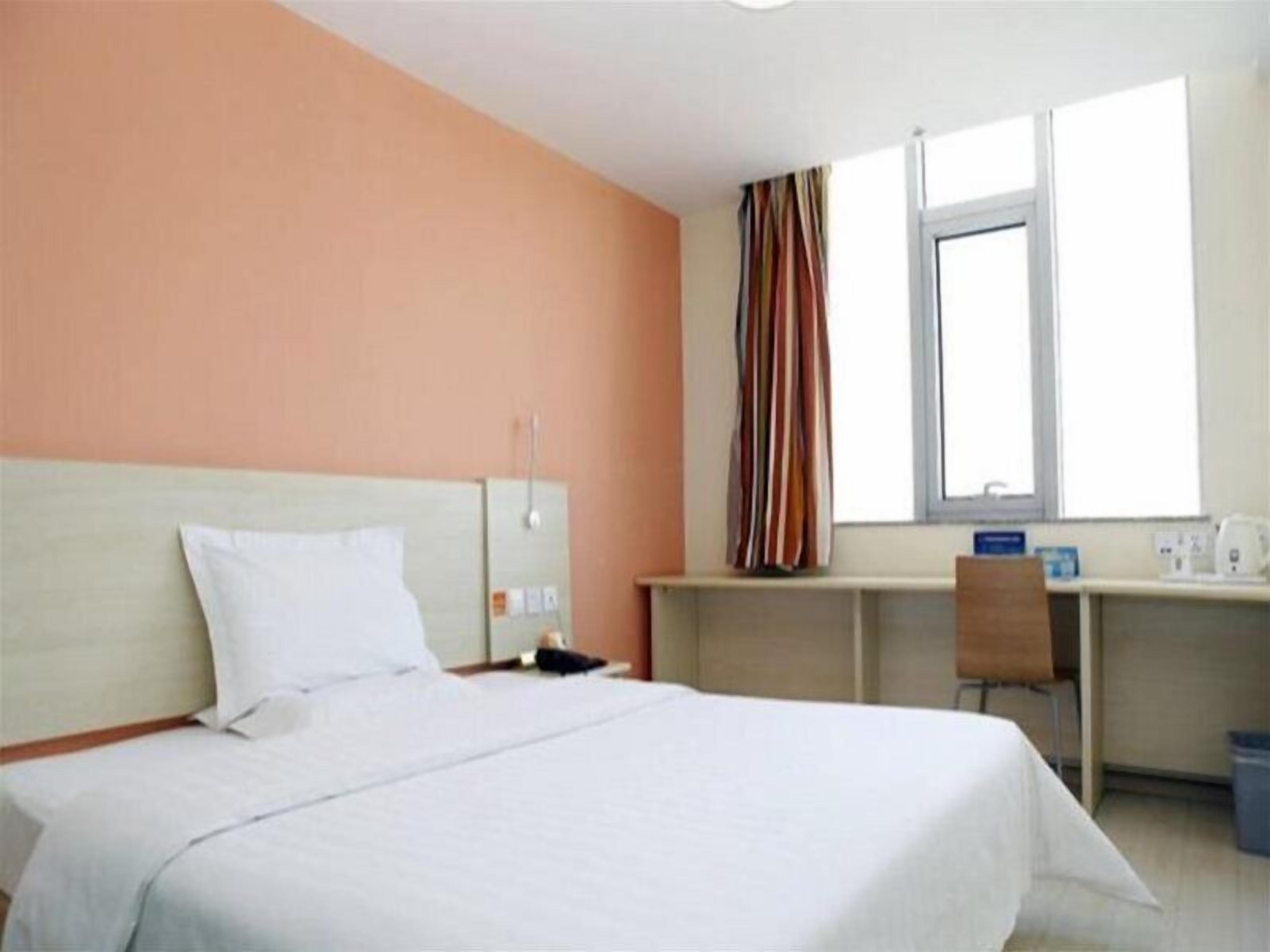 Ein Hotelzimmer mit Bett, Schreibtisch, Stuhl, einem Fenster mit Vorhängen und einem kleinen Tisch mit Wasserkocher.