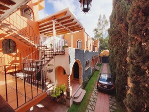 A courtyard with a staircase leading to a balcony, a car parked nearby, and a building with arched windows and a tiled roof. - Villa Alfonsina (Mexico City)