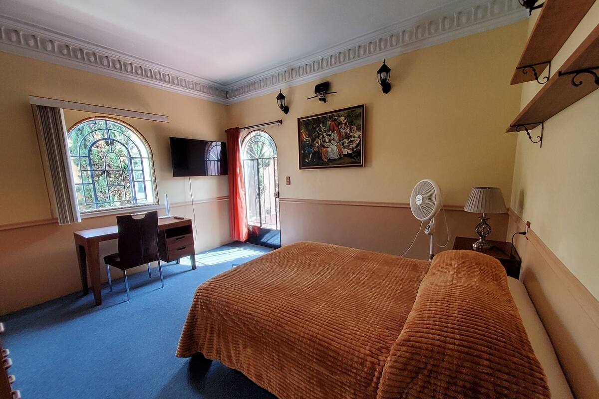 Habitación de hotel con cama, escritorio, silla, televisor y un cuadro en la pared.