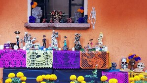 A table with colorful papel picado and marigold flowers, decorated with various Day of the Dead figures and ornaments. - Villa Alfonsina (Mexico City)