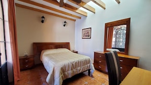 A bedroom with a wooden ceiling, a bed, a desk, a chair, and a window with a decorative frame. - Villa Alfonsina (Mexico City)
