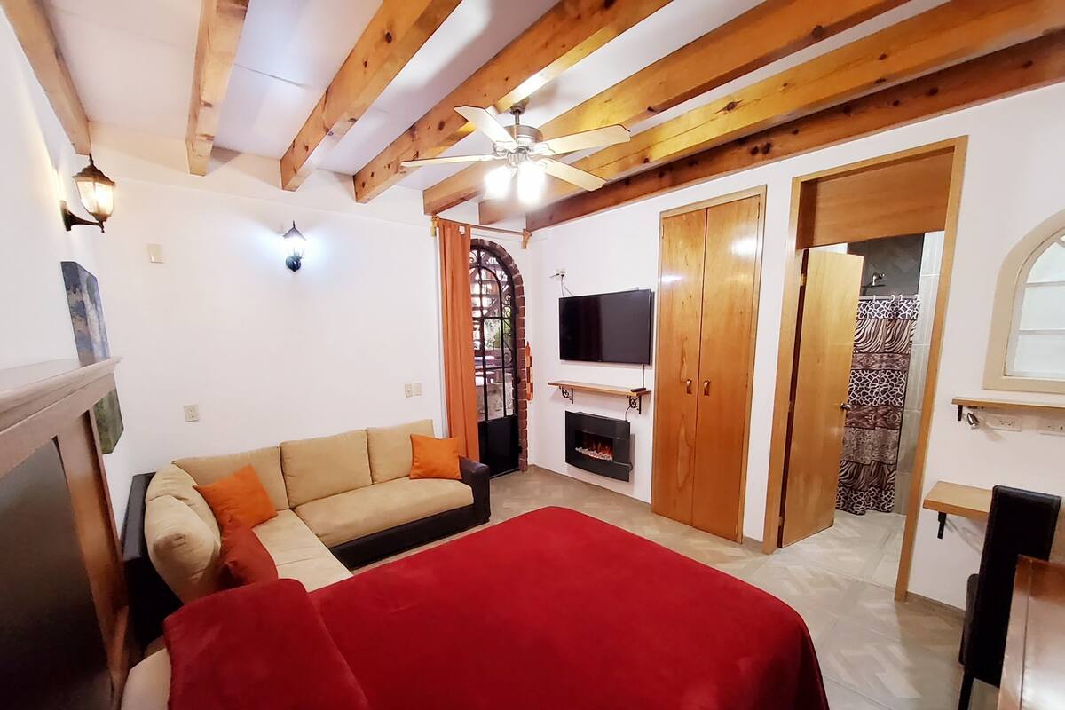 Un salón acogedor con un sofá, una manta roja, un televisor y vigas de madera en el techo.
