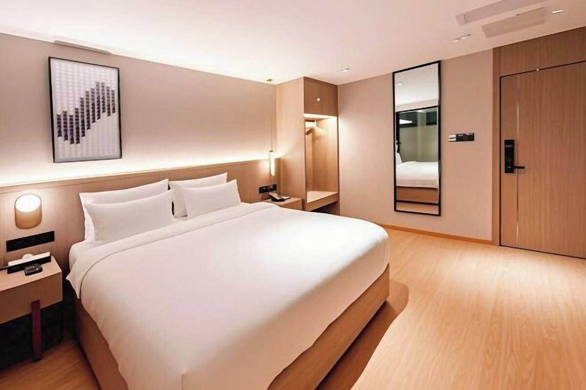 Ein modernes Hotelzimmer mit einem großen Bett, Nachttischen, einem Spiegel und einem Kleiderschrank.