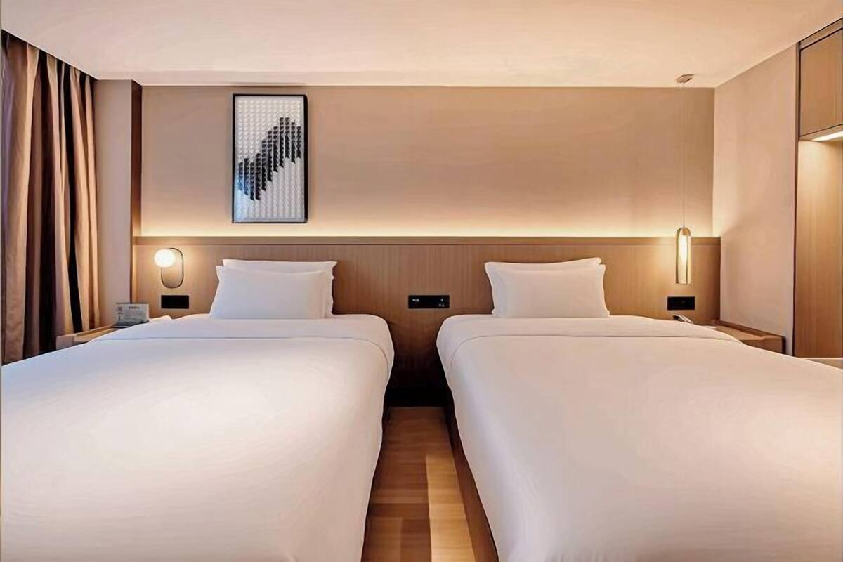 Ein Hotelzimmer mit zwei Betten, einem gerahmten Kunstwerk darüber, Nachttischlampen und Holzboden.