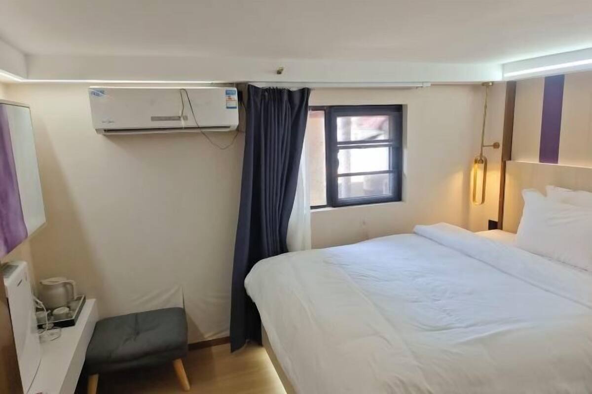 Ein Hotelzimmer mit Bett, Schreibtisch mit Stuhl, Fenster mit Vorhängen, Klimaanlage und einer Wandleuchte.