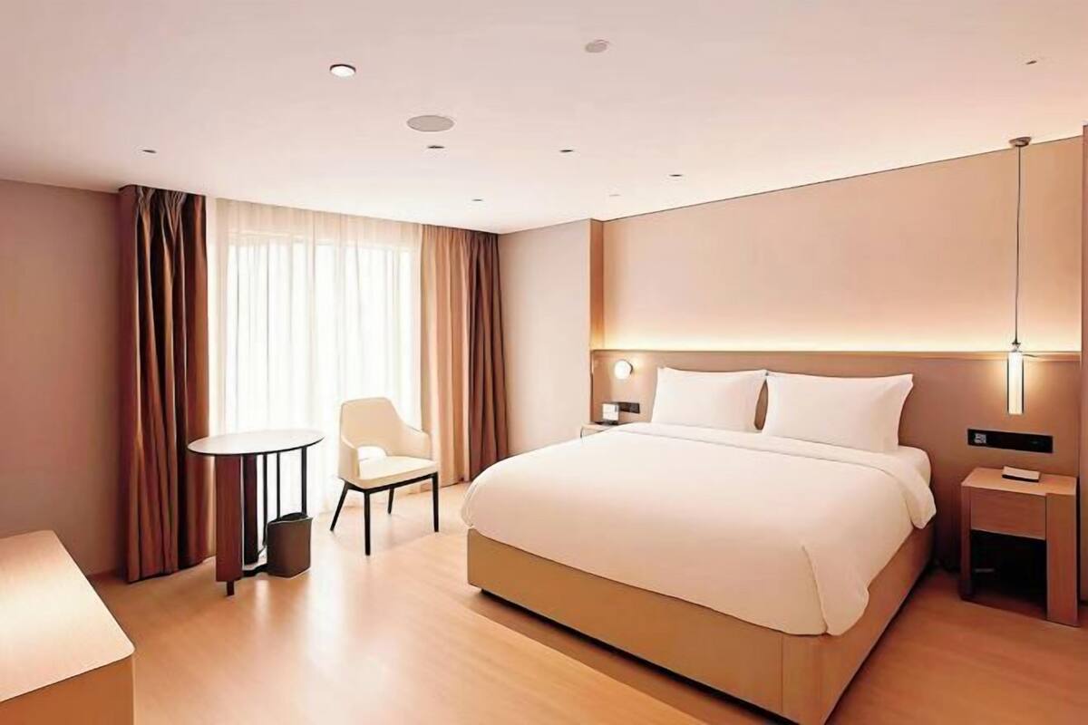 Ein modernes Hotelzimmer mit einem großen Bett, einem kleinen Tisch, einem Stuhl und einem Nachttisch.