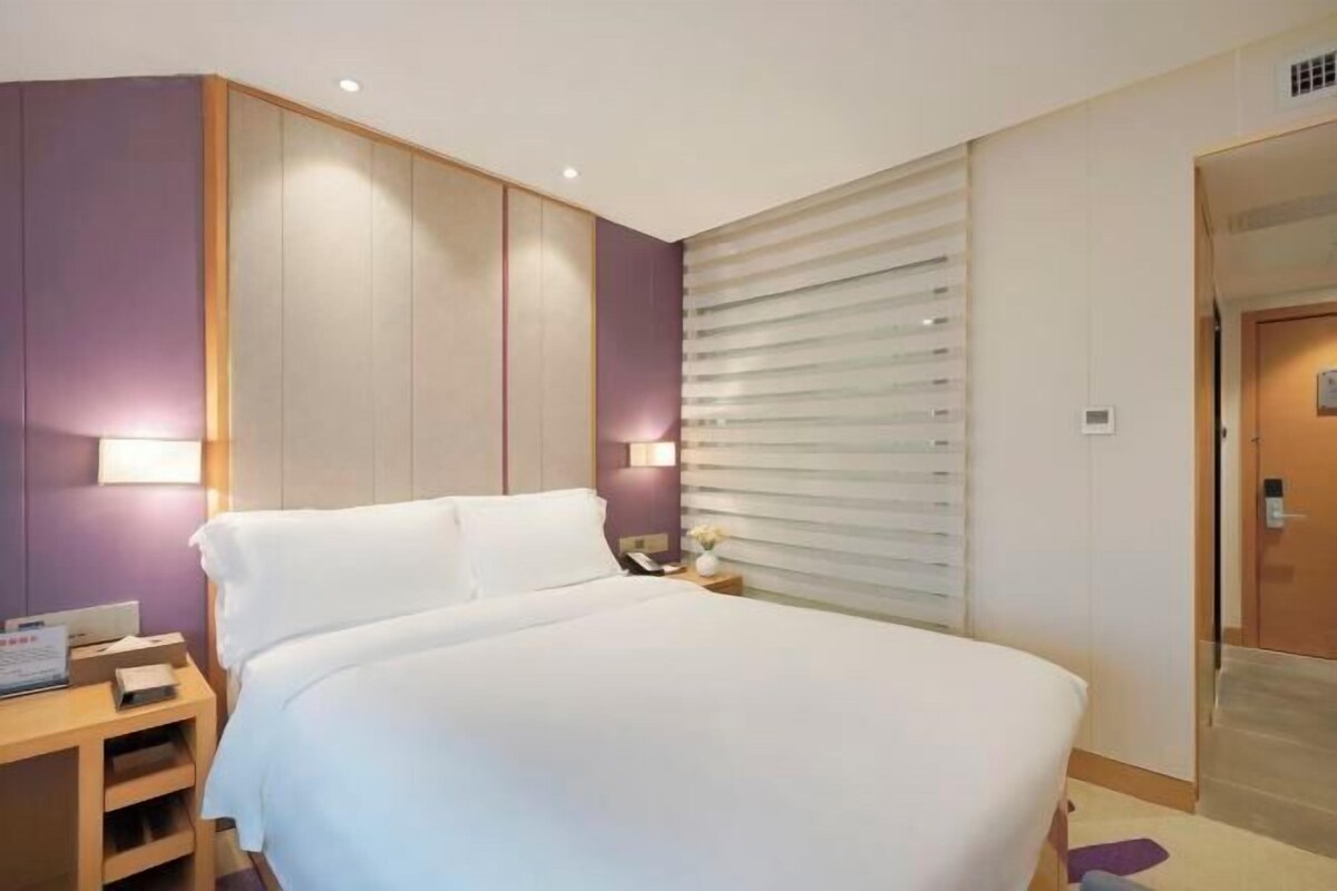 A hotel room with a large bed, bedside tables, and a window with blinds.