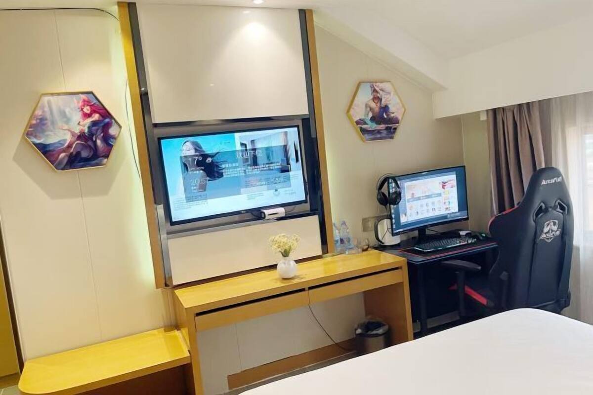 Ein Hotelzimmer mit einem großen Flachbildfernseher, einem kleineren Bildschirm, einem Gaming-Sessel und einem Holztisch.