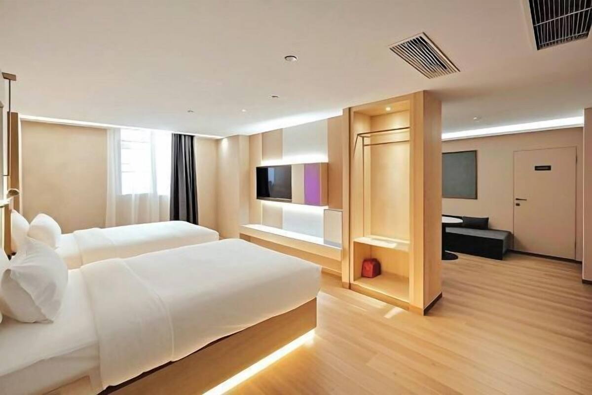 Ein modernes Hotelzimmer mit zwei Betten, einem Fernseher, einem Schreibtisch und einer Sitzecke.