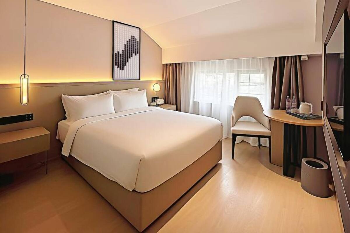 Ein modernes Hotelzimmer mit einem großen Bett, Nachttischen, einem Schreibtisch mit Stuhl und einem großen Spiegel.