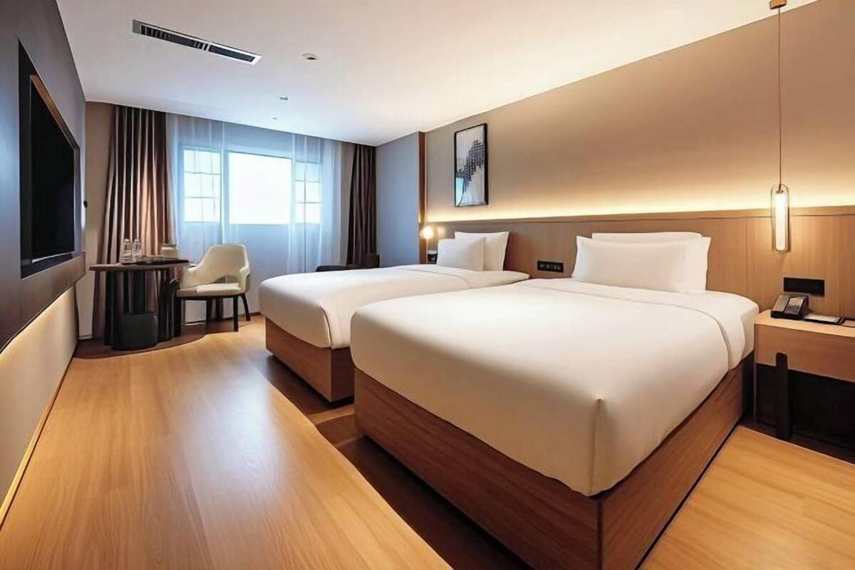 Ein Hotelzimmer mit zwei Betten, einem Schreibtisch, einem Stuhl, einem Fernseher und einem großen Fenster.