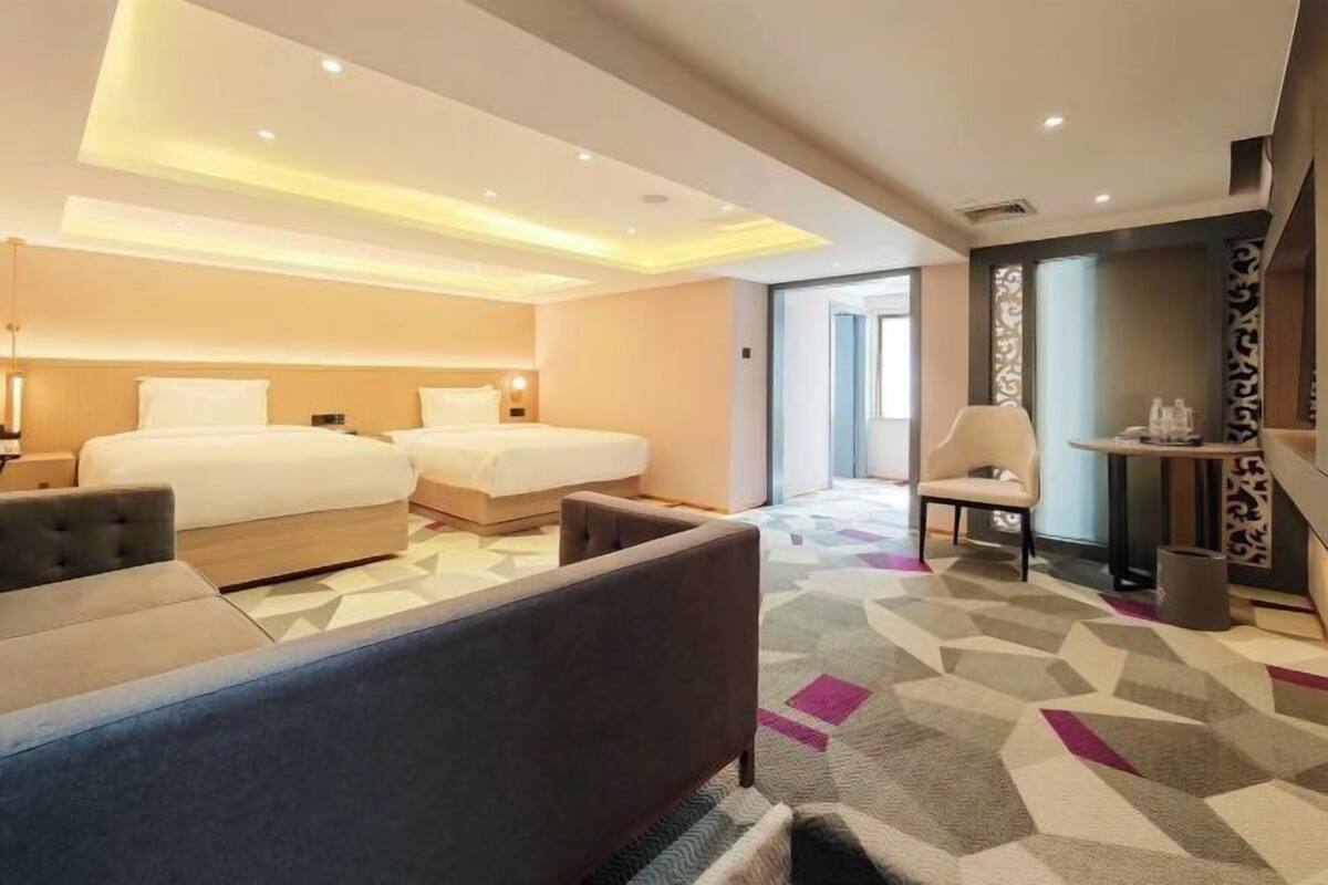 Ein Hotelzimmer mit zwei Betten, einem Schlafsofa, einem kleinen Tisch und einem Stuhl.