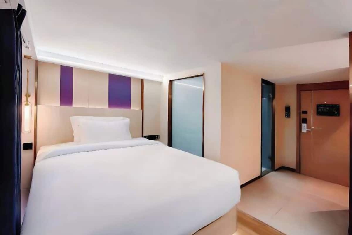 Ein modernes Hotelzimmer mit einem großen Bett, einem Nachttisch, einer Wandleuchte und einer Tür mit Zahlenschloss.