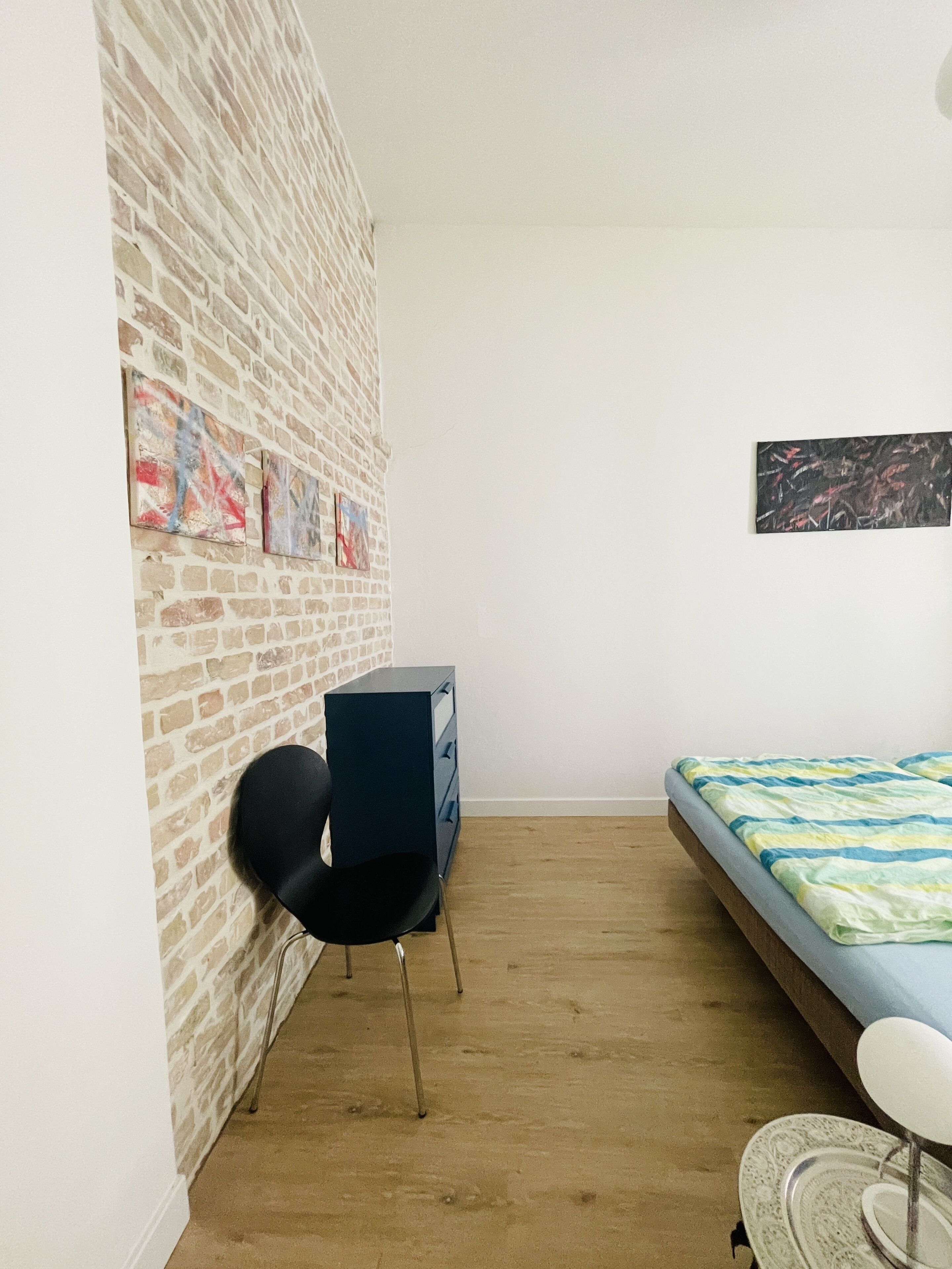 Une pièce avec un mur en briques, un lit recouvert d’une couvre-lit à motifs, un bureau avec une chaise et une commode.