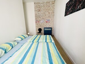Una habitación pequeña y acogedora con pared de ladrillo, cama con ropa de cama a rayas, una silla y una mesita.