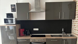 A compact kitchen with a microwave, stove, oven, and sink. There is a dining table with a chair, and a brick wall on one side.
