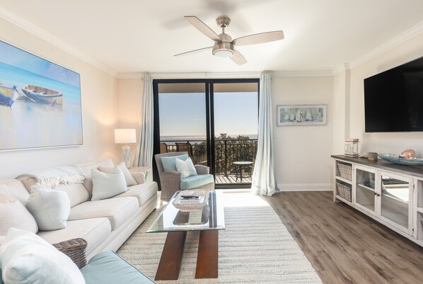 A living room with a sofa, coffee table, and a TV. There is a balcony with a view. - Oceanfront, Newly Renovated, Luxury Two-Story Penthouse - Shipwatch 418 (Isle of Palms)