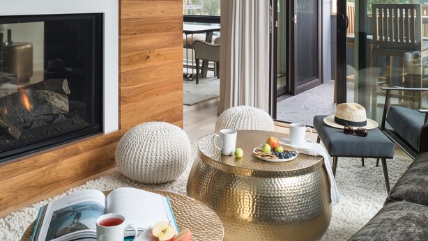 Una sala de estar moderna con chimenea, mesas de centro redondas y un balcón con mobiliario de exterior.